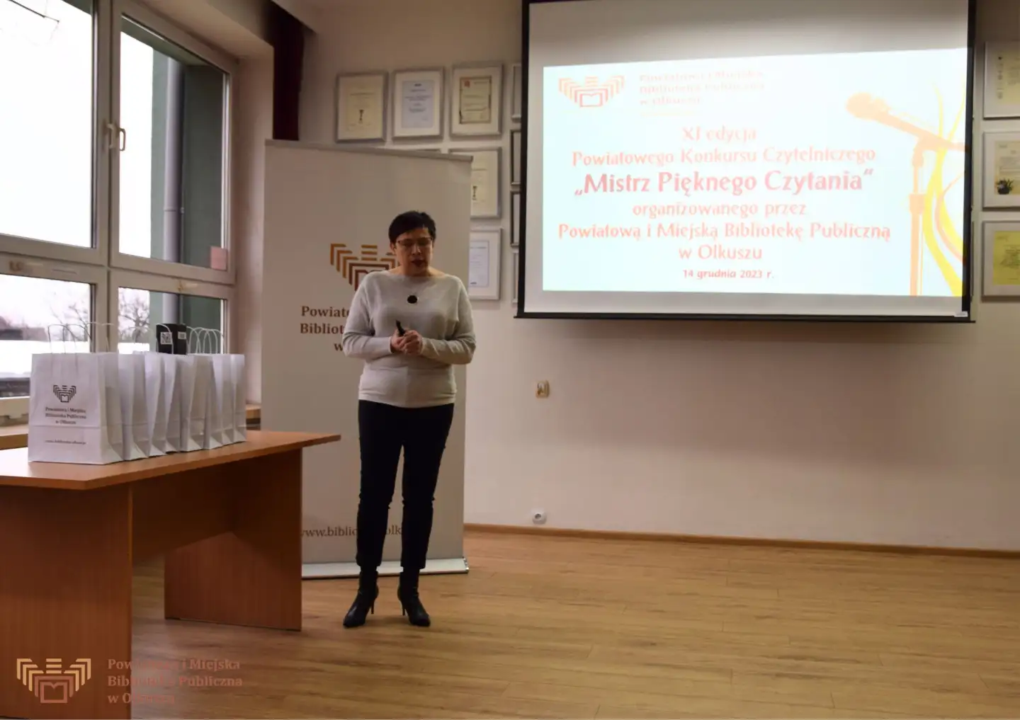 Zdjęcie zostało zrobione w Czytelni Biblioteki. Przedstawia Panią Dyrektor mówiącą do zgromadzonych słuchaczy.