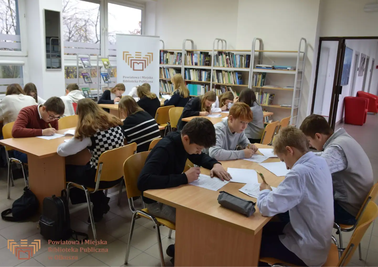 Zdjęcie zostało zrobione podczas konkursu literackiego "Z polszczyzną za Pan brat". Przedstawia dzieci siedzące przy stoliku i rozwiązujące zadania konkursowe.